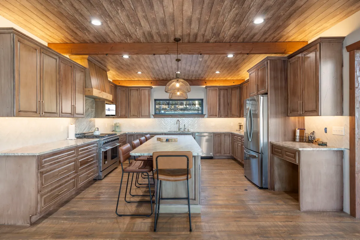The chef’s kitchen is featured here with a large island, bar stools, stylish pendant lighting, and sleek stainless steel appliances, all set in a spacious open-concept layout. The clean design and inviting mood make it an ideal space for cooking and connection.