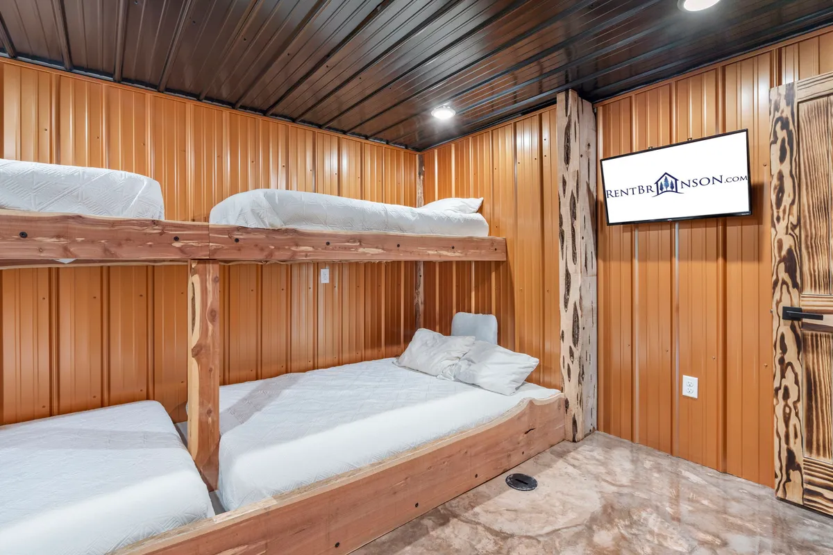 A spacious bunk room with two sets of wooden bunk beds, cozy bedding, and a TV screen, all set against stylish wooden accents. The space feels casual and welcoming—ideal for children, cousins, or groups of friends to relax and bond.