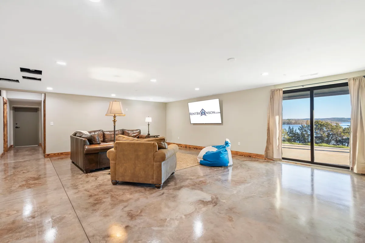 A lower-level living space featuring a comfortable sofa, bean bag chair, large window with stunning lake views, and a television. The room is designed for casual gatherings, movie nights, or quiet moments with a view.