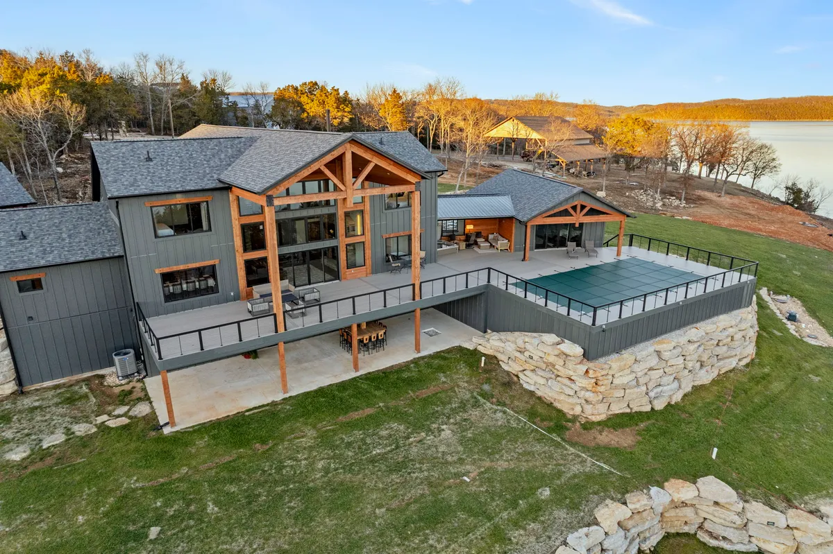 This image captures an expansive deck overlooking Table Rock Lake, complete with a pool area, wooden beams, and a natural stone wall. Outdoor lounge furniture invites guests to relax and take in the sunset views, while the setting evokes a sense of tranquility and privacy.